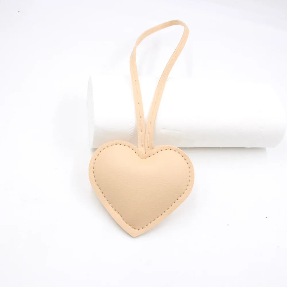 A light tan PU leather heart-shaped keychain with a loop for attachment.