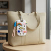 A beige canvas tote bag with a white charm keyring featuring a rainbow, stars, and clouds.