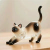 A clear glass figurine of a cat with brown and black markings sitting on a wooden surface.