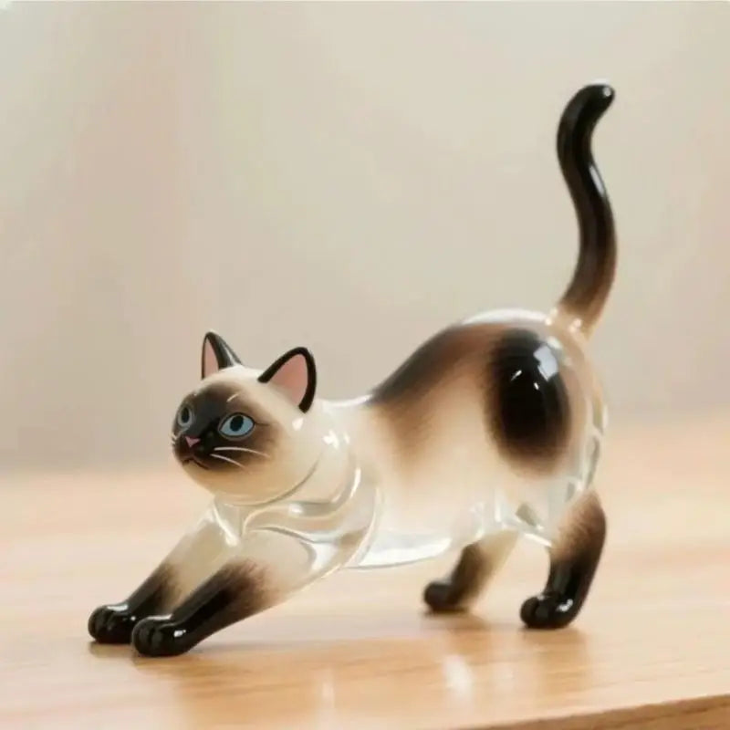 A clear glass figurine of a cat with brown and black markings sitting on a wooden surface.