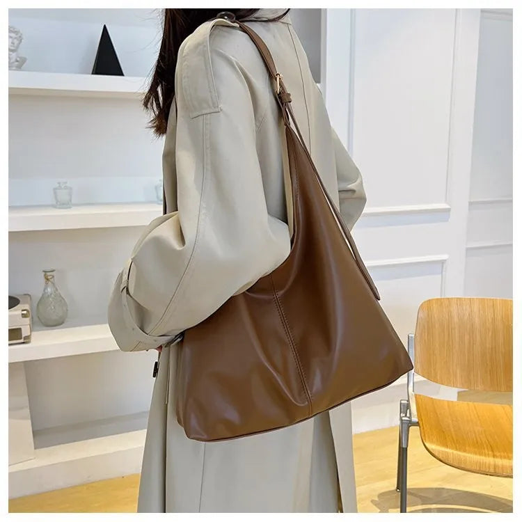 Eine Frau hält eine braune Retro-Canvas-Tasche in einem hellbeigen Mantel vor weißem Hintergrund.