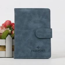 A dark blue leather passport holder with a flap, resting next to a small potted pink flower arrangement.