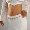A woman wearing a white knitted top and skirt, accessorized with a vintage gold plated sunflower smiley face waist chain.