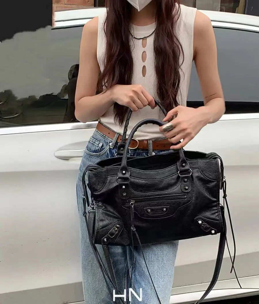A woman holds a black saddle-shaped PU leather city tote bag in front of a white car.
