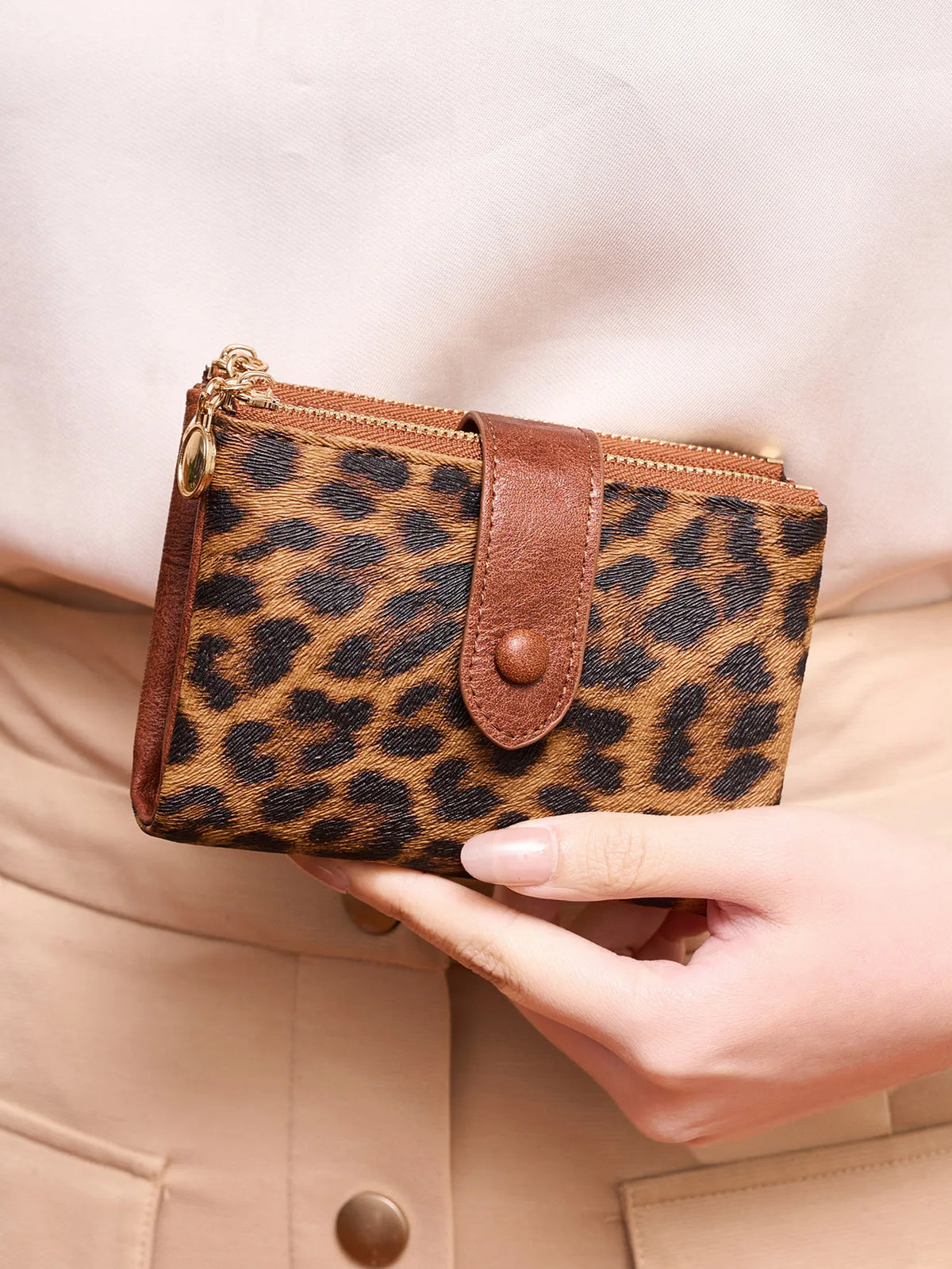 A brown leopard print women's wallet is held against a beige jacket.