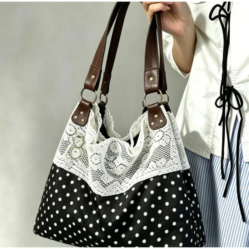 A close-up of a black and white polka dot patchwork shoulder bag with white lace trim being held by a hand.