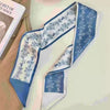 Foulard pour cheveux en soie élégant, floral blanc et bleu, drapé sur un tissu clair.