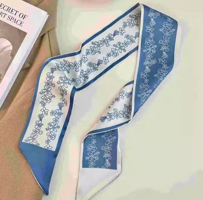Foulard pour cheveux en soie élégant, floral blanc et bleu, drapé sur un tissu clair.