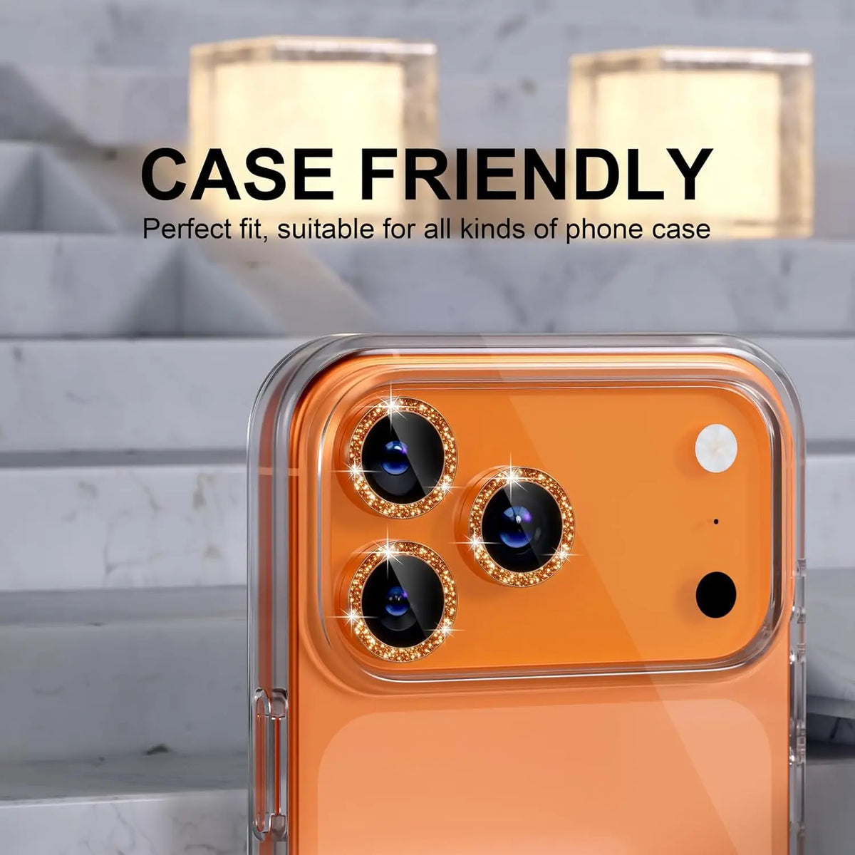 An orange iPhone is shown with a glitter diamond camera lens protector and metal frame installed.