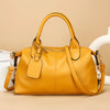 A mustard yellow soft leather tote bag with a top handle and adjustable strap resting on a light surface.