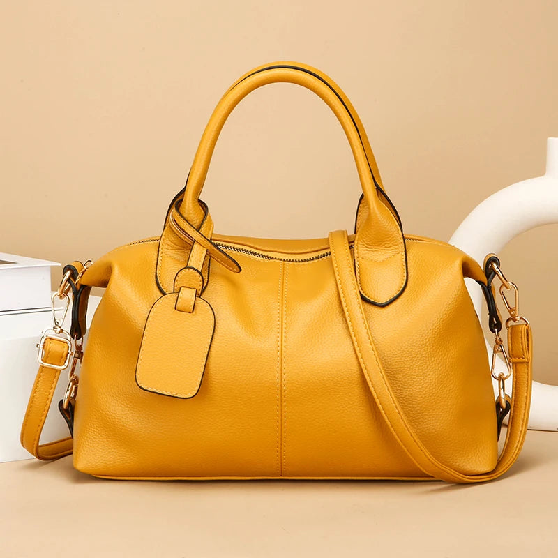 A mustard yellow soft leather tote bag with a top handle and adjustable strap resting on a light surface.