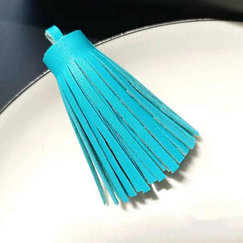A bright turquoise leather tassel fringe craft supplies set displayed on a white plate.