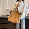 A woman wearing a white sweater holds an orange canvas tote bag in front of a dark cabinet.
