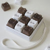 A set of brown and white kawaii cat keycap fidget toys arranged in a white rectangular holder with a white elastic string.