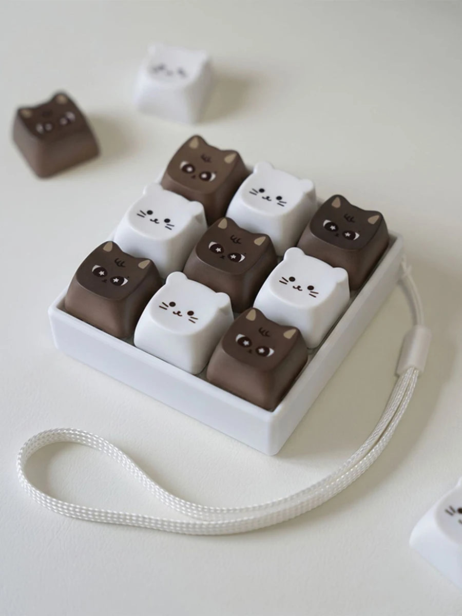 A set of brown and white kawaii cat keycap fidget toys arranged in a white rectangular holder with a white elastic string.