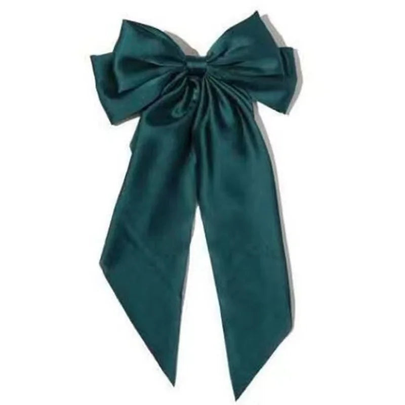 A dark teal silk bow accessory used as a hair clip or bow for a ponytail.