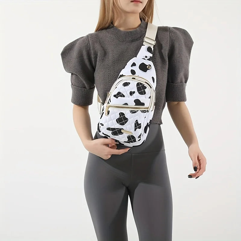 A woman wearing a gray sweater and dark leggings holds a white quilted crossbody sling bag with a black cow print pattern.