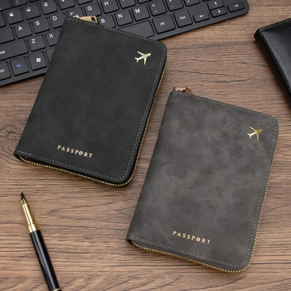 A black passport wallet with gold stitching and a small airplane emblem is shown next to a laptop keyboard and a pen on a woo
