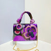 A purple and pink sequin embroidered floral clutch bag with a purple fabric strap and gold chain.