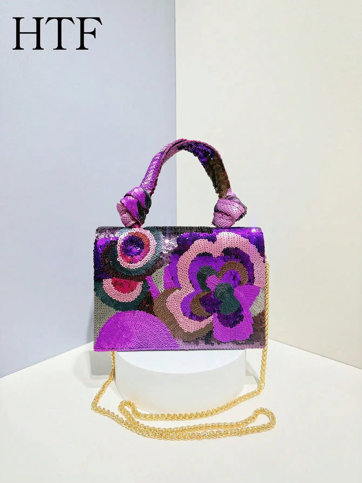 A purple and pink sequin embroidered floral clutch bag with a purple fabric strap and gold chain.