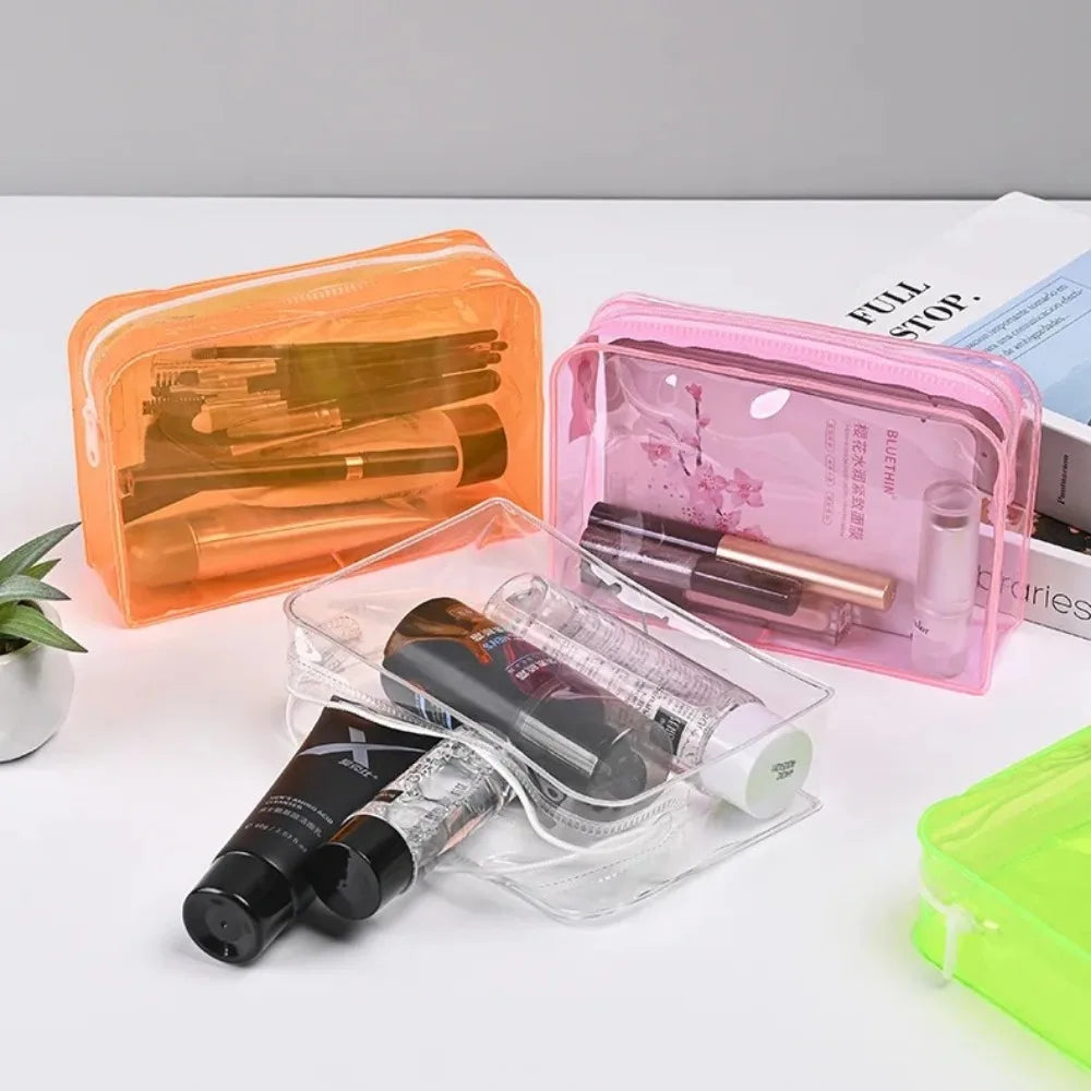 A set of transparent PVC travel makeup bags in orange and pink colors with various cosmetic items inside.
