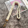 Cremfarbener, geraffter Lanyard mit goldenem Schlüsselclip auf grauer Oberfläche neben einem Foto.