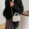 A woman holds a white pearl beaded clutch bag with a long strap against a black top and gray skirt.