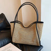 A straw woven tote bag with black PU trim and matching pouch resting on a black leather sofa.