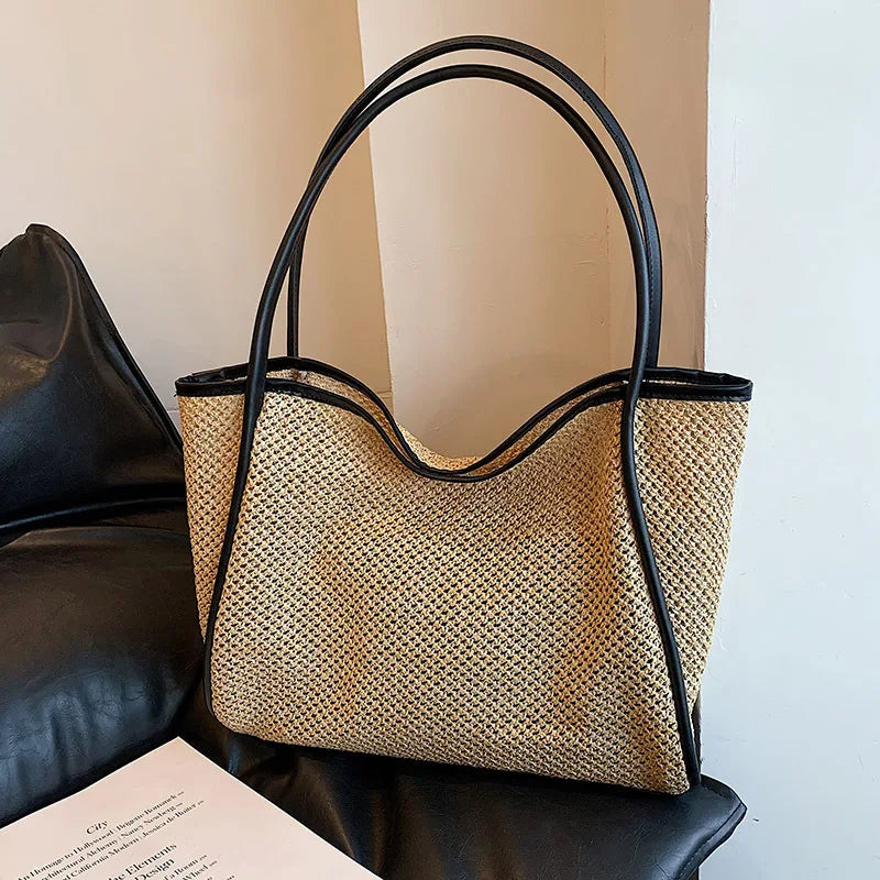 A straw woven tote bag with black PU trim and matching pouch resting on a black leather sofa.