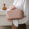 A person holds a light pink foldable cosmetic storage bag against a white shirt and brown skirt.