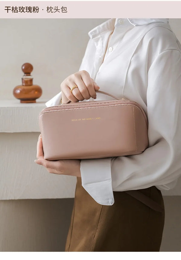 A person holds a light pink foldable cosmetic storage bag against a white shirt and brown skirt.