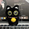 Colgante de peluche de gato negro sobre el teclado de una laptop.