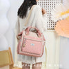 Une femme porte un sac isotherme en cuir rose et matelassé sur son épaule, vêtue d'un pull tricoté clair.