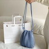 A light blue PU leather pleated crossbody bag is being held by a hand, placed in front of white paper shopping bags.