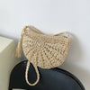 A light beige handmade rattan straw crossbody bag hanging against a white wall.