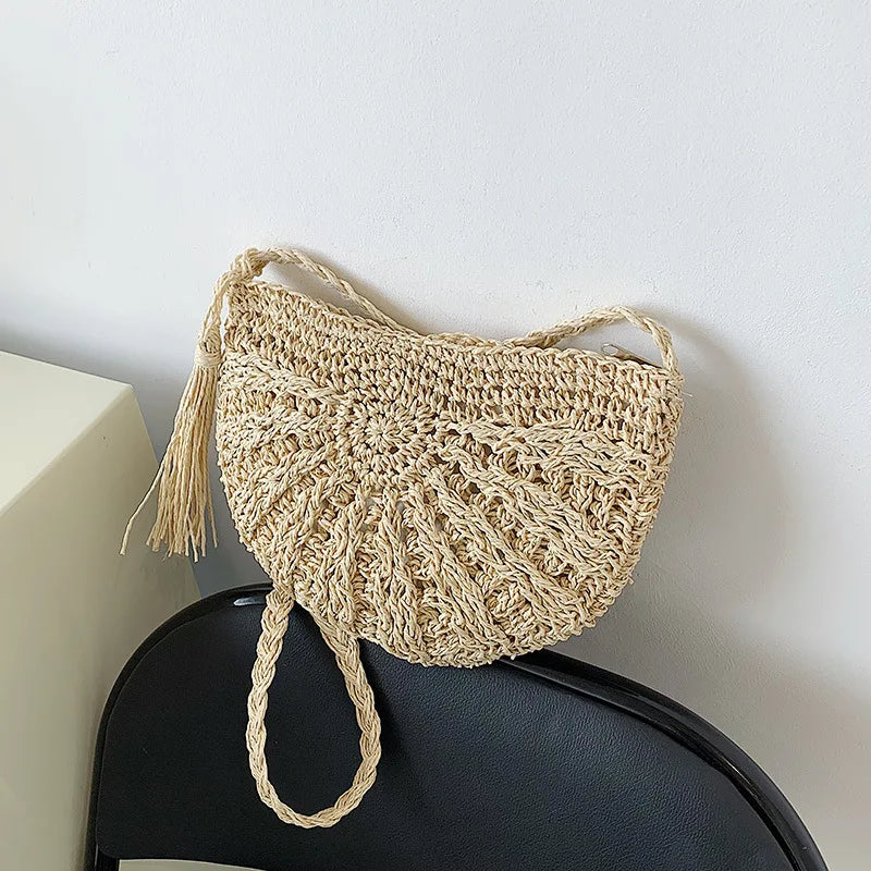 A light beige handmade rattan straw crossbody bag hanging against a white wall.