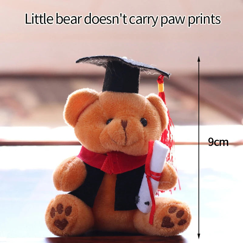 A fluffy brown teddy bear wearing a graduation cap, red ribbon, and holding a white camera.