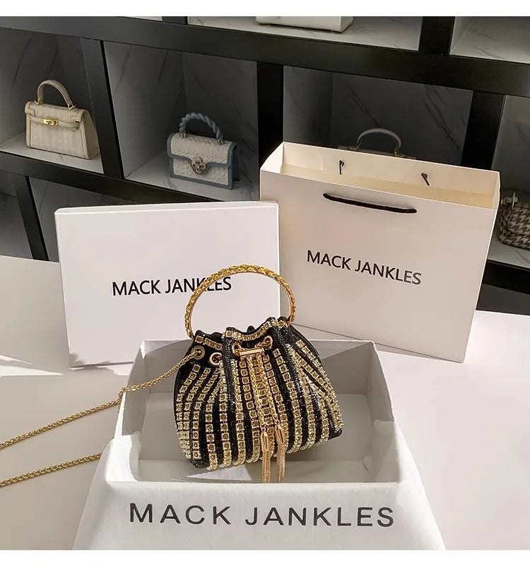 A gold chain embellished evening clutch displayed in a white box with the Mack Jenkins brand visible.