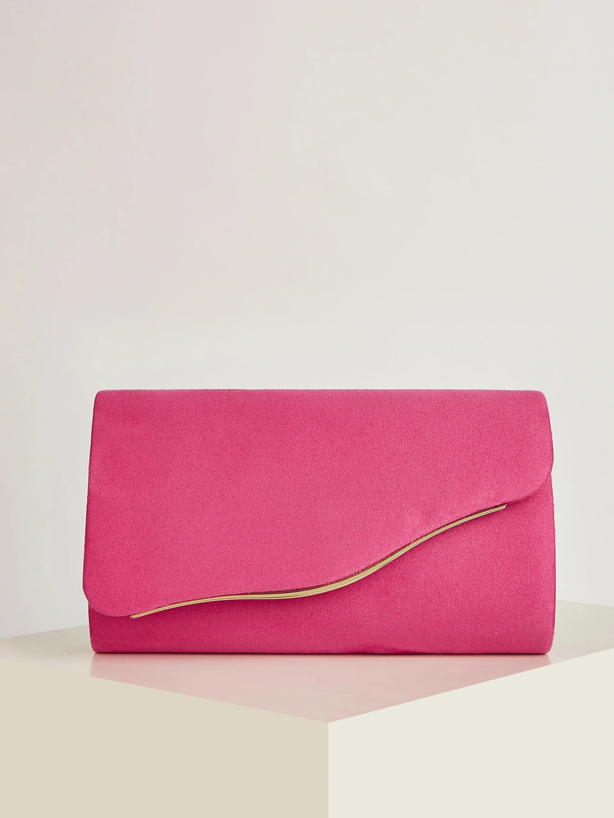 A vibrant pink velvet evening clutch with a visible yellow lining resting on a white surface.