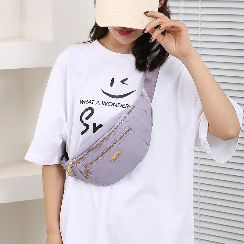 Une femme portant un t-shirt blanc tient un sac banane waterproof violet avec des accents dorés.