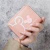 A hand holds a pink cartoon-themed mini zipper coin purse featuring a white Mickey Mouse silhouette and glitter accents.