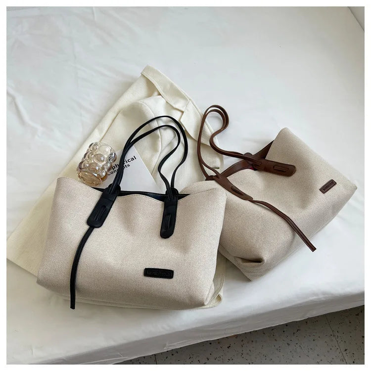 A beige canvas shoulder tote bag with brown leather straps resting on a white surface.