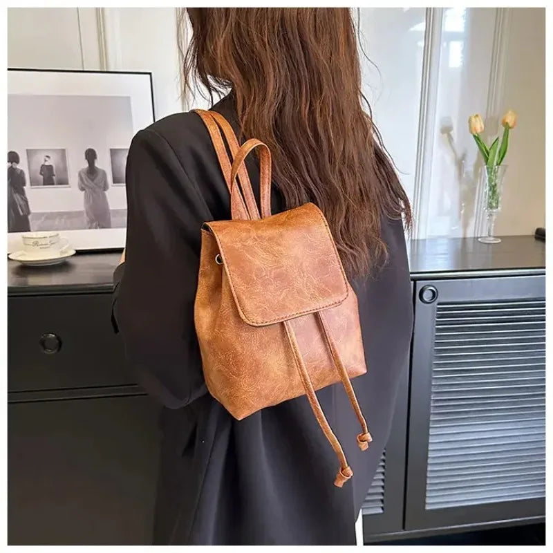 Une personne tient un mini sac à dos à cordon marron rétro sur un fond sombre.