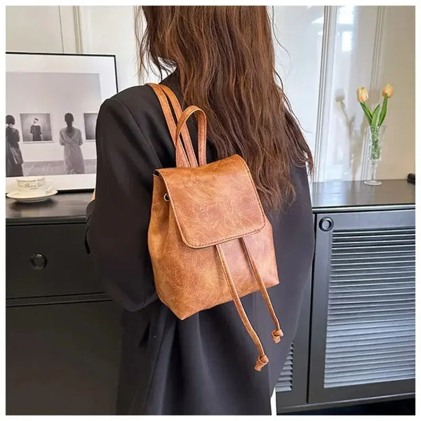 Eine Person hält einen retro braunen, mit Schnur verschlossenen Mini-Rucksack vor einem dunklen Hintergrund.