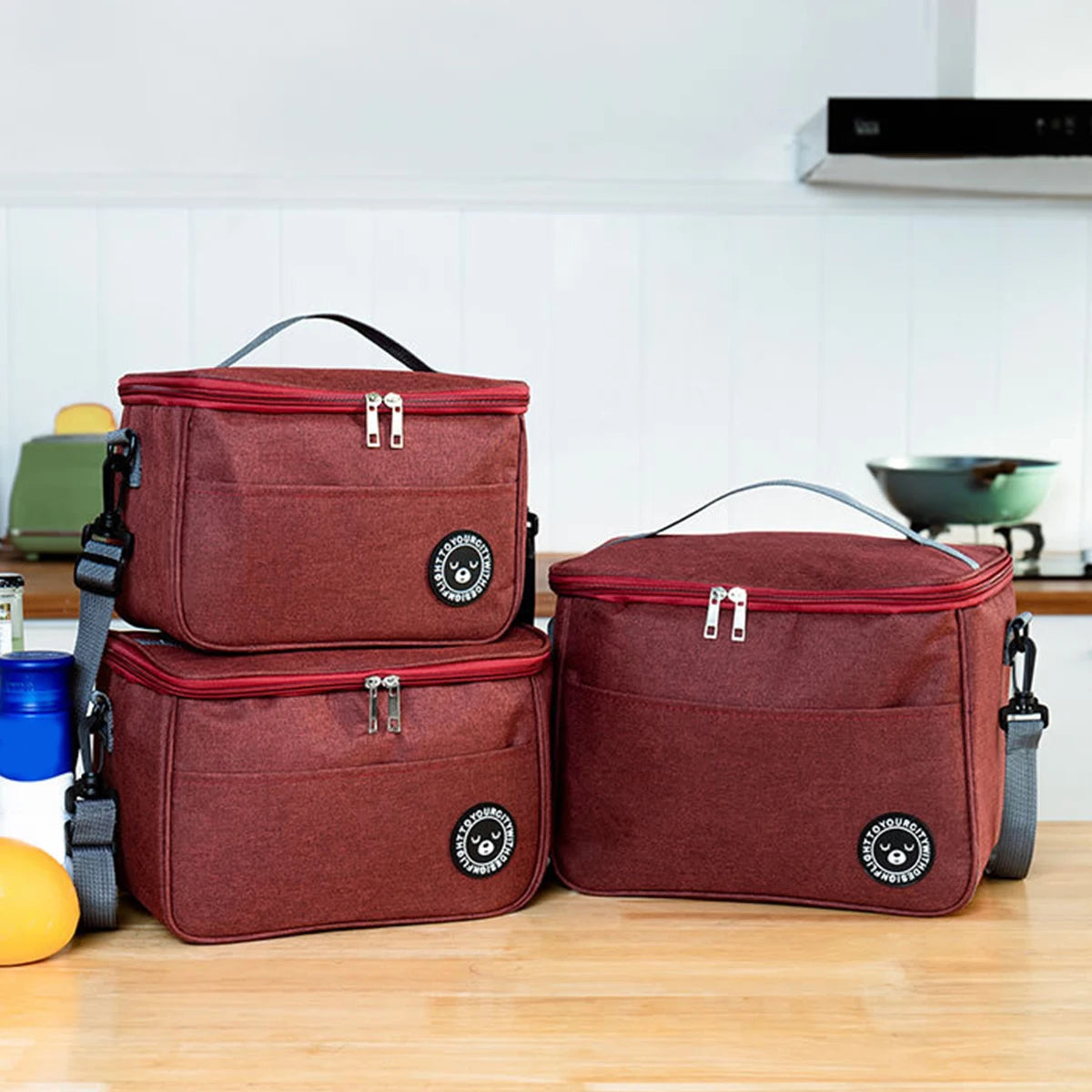 Two maroon insulated lunch tote bags with adjustable shoulder straps resting on a wooden surface.