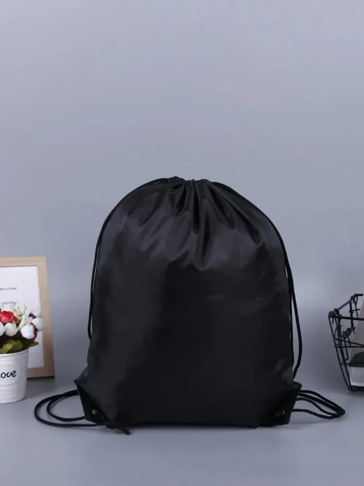Black gym drawstring backpack with multiple pockets lying on a gray surface.