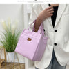 A person holds a pink insulated lunch bag against a white blazer in a bright indoor setting.