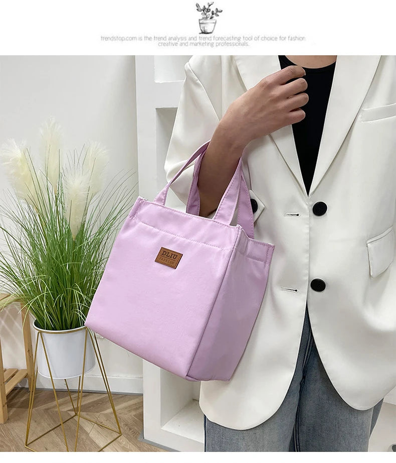 A person holds a pink insulated lunch bag against a white blazer in a bright indoor setting.