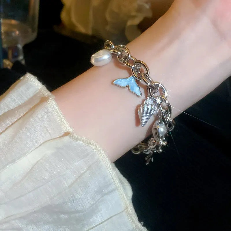 A close-up of a silver charm bracelet featuring an ocean pearl, a blue starfish, and a seashell accent on a wrist.