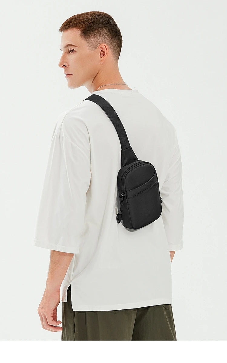 Un hombre vistiendo una camiseta blanca y pantalones oliva sostiene un bolso cruz multifuncional negro.